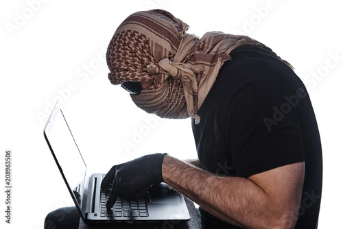 Fotografía The man hidden under the arafatka and black glasses keeps his hands in black gloves on the laptop