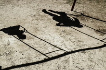 Children Ride On A Swing. Only The Shadow Of Two Children Is Visible. Kids Swing Synchronously.