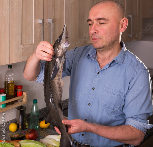 Positive man standing holding uncooked sturgeon Poster