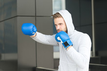 Man Athlete On Concentrated Face With Sport Gloves Practicing Boxing Punch, Urban Background. Training His Boxing Skills. Boxer Hood Head Practices Jab Punch. Sportsman Boxer Training Boxing Gloves