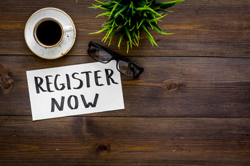 Poster - Membership concept. Template for registration. Register now hand lettering iconon word desk with glasses, coffee, plant on dark wooden background top view space for text