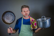 © TheVisualsYouNeed - young attractive stressed and overwhelmed lazy man with apron holding kitchen pan and cook pot in stress and frustrated isolated background in domestic work and messy house husband