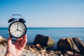 Hand hold watch on beach background.Alarm clock on sea and sand background different time with summer vacation.Vacation time concept.