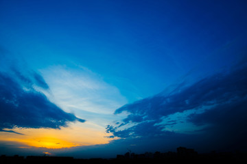 Wall Mural - atmospheric blue cloudy sky behind silhouettes of city buildings. cobalt and orange background of su