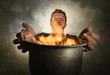 © TheVisualsYouNeed - young attractive and shocked messy home cook man with apron holding cooking pot in fire burning the food in kitchen disaster