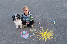 Young Boy Child Lovingly Hugs Pet Dog Lapdog. Copy Space. Happy Little Kid Siting On Asphalt Sidewalk, Drawing Colored Chalk On Outdoors.Smiling Looking At The Camera, Top View. Friendship With Puppy.