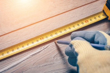 Wall Mural - A worker with a construction measuring tape makes measurements on a wooden floor