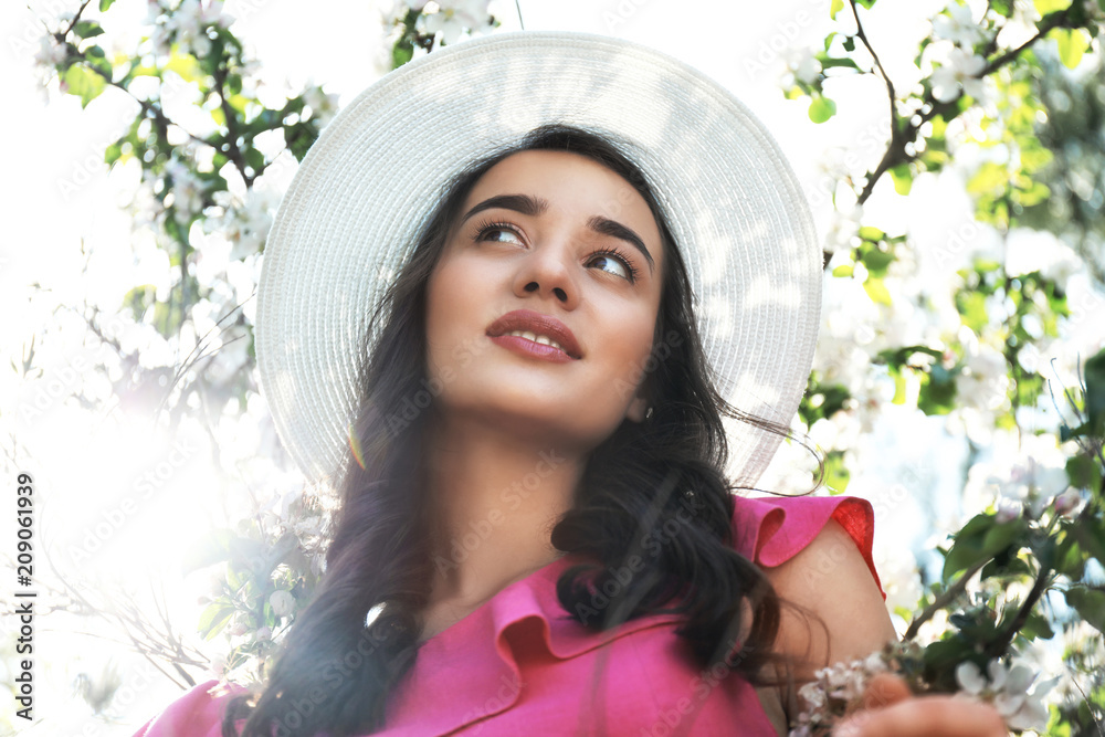 Beautiful young woman near blossoming tree on sunny spring day