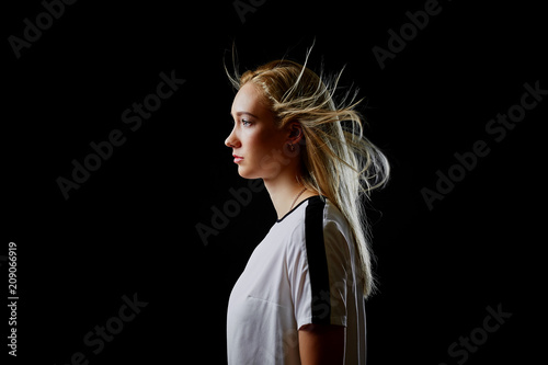 Fotografía Portrait in profile of a beautiful blonde girl in a sports t-shirt on a black background