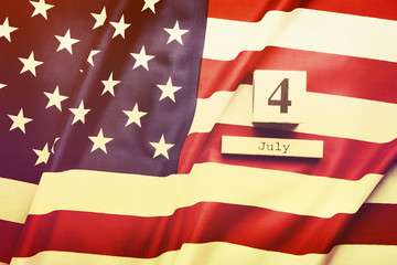 Wall Mural - Ruffled American flag and wooden cube calendar with 4th of July, USA Independence Day date, copy space celebratory background. US festive composition, top view, close up. Retro tone, vintag filter