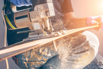 The electric jigsaw in the hands of the worker, the sawdust and dust are flying beautifully, shooting in motion