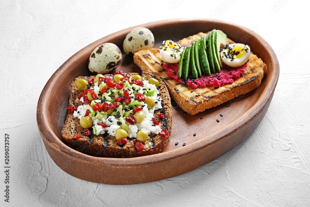 Plate with tasty toasts on light background