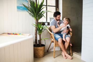 Wall Mural - Father and a toddler boy sitting on a chair and brushing their teeth at home.