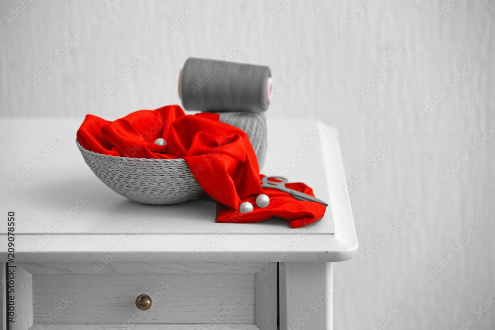 Basket with color fabric and sewing accessories on table against light background