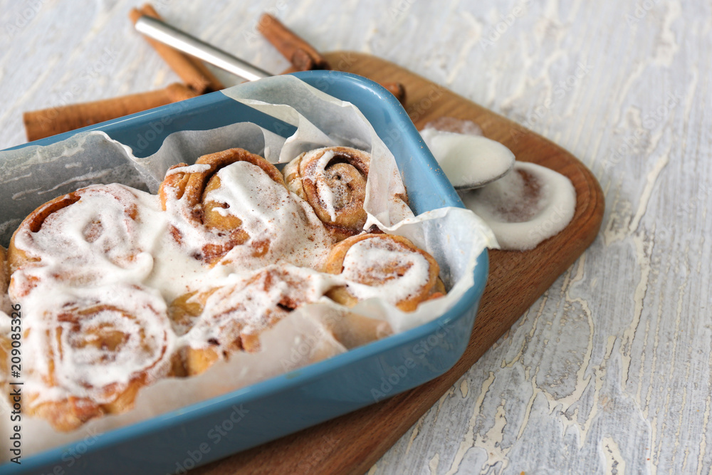 Baking dish with delicious cinnamon buns on wooden background, closeup