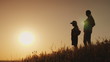 © StockMediaSeller - Silhouettes of a woman with a child. They stand with backpacks behind their back, they admire the sunset. Traveling together concept