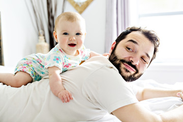 Young happy father playing with babyon bed