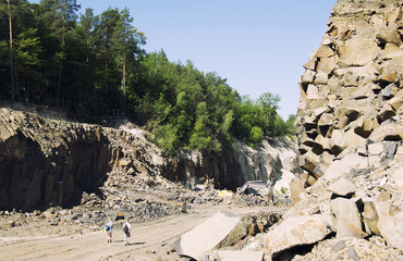 Two tourists go along the trail in a basalt career. Woman and man near basalt rocks. Ukraine. Ancient volcano.