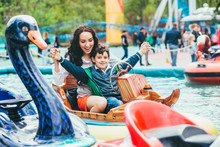 A Happy Mother And Son Are Riding On A Merry-go-round Carousel Together, Smiling And Having Fun At A Fair Or Amusement Park.