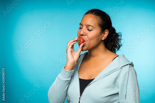Fotografia Beautiful young mixed race woman in casual clothing eating and enjoying a fresh