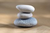 Fototapeta Desenie - Group of zen stones pile, grey meditation pebbles tower on light brown wooden background in sunlight