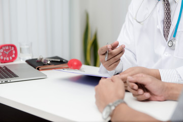 Wall Mural - Doctor and patient are discussing something with young man patient and making notes while sitting at medical consultation.