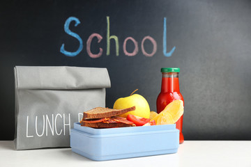 Appetizing food in lunch box and bag on table near chalkboard with word SCHOOL