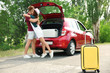 Young couple with suitcases packed for summer journey near car