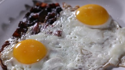 Wall Mural - Sprinkle Sea Salt And Ground Black Pepper Over Fried Eggs And Bacon - Close Up View