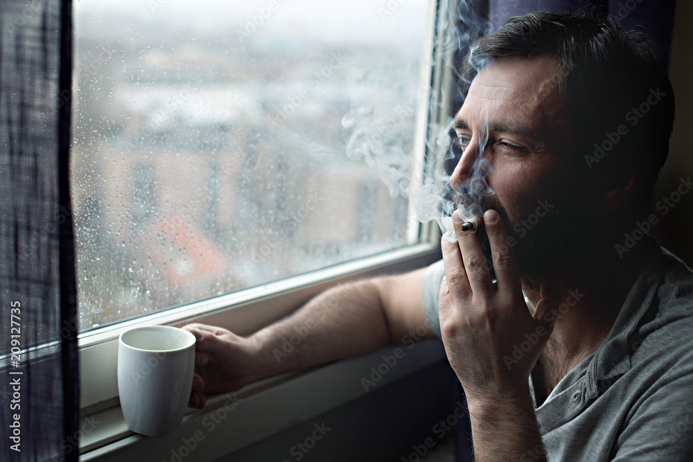 cigarette window Man with morning coffee cup smoking cigarette by the window Stock Photo