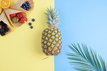  A tropical fruit is a pineapple and a palm branch on a yellow blue background, a variety of sweet berries. Free space for text. Copy space, flat lay.