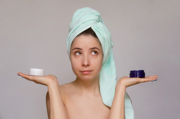 Woman holding a two jars with various cream of facial mask in her hands and comparing it. Skin care treatment concept.