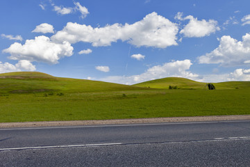 Wall Mural - Road in the field, long distance trail in the field. Beautiful green hills. Blue sky with fluffy clouds