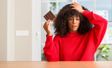 Poster - African american woman eating chocolate bar at home stressed with hand on head, shocked with shame and surprise face, angry and frustrated. Fear and upset for mistake.