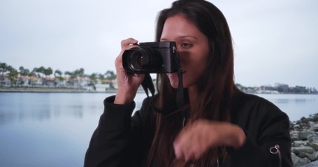 Wall Mural - Hipster girl in bomber jacket standing on rocky coast taking picture of the ocean, Millennial female with dslr camera taking photograph by the water, 4k