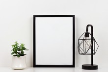 Mock Up Black Frame, Succulent Plant And Industrial Style Lamp On A Shelf Or Desk. White Shelf And Wall. Portrait Frame Orientation.