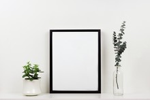 Mock Up Black Frame With Plant And Branches On A Shelf Or Desk. White Shelf And Wall. Portrait Frame Orientation.