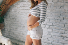 Pregnant Woman Posing In Front Of A White Brick Wall