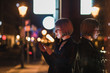 © IraEfremova/Stocksy - Blond woman with short hair using her smartphone on the street in the evening city.