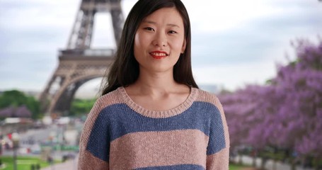 Wall Mural - Happy millennial woman with big smile wearing a blue-striped sweater in front of Eiffel Tower, Close up of young attractive Asian tourist smiling for camera in Paris France, 4k