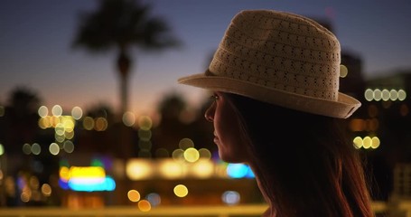 Wall Mural - Silhouette of woman on rooftop admiring view of city lights at night, Close up of pensive female in fedora looking out at cityscape, 4k