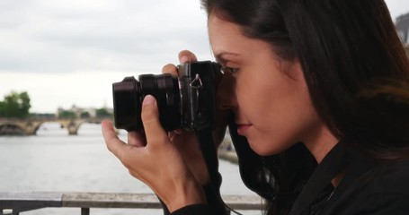 Wall Mural - Side view of millennial woman on bridge over the Seine taking photo with dslr camera, Young travel photographer focuses lens and takes picture while on vacation in Paris, 4k