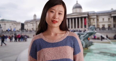 Wall Mural - Pleasant young woman with happy expression and wearing a casual sweater in front fountain at Trafalgar square, Close up of joyful millennial female in London UK, 4k