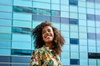 © guille Faingold/Stocksy - Pretty businesswoman with afro smiling over glass building.