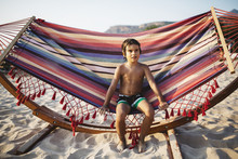 6 Year Old Boy Sitting On A Hammock On The Beach