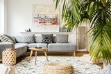 Fototapeta Boho - Pouf and wooden table in modern living room with painting above grey corner couch. Real photo