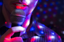 Young Man Singing With A Microphone With Colorful Background Lights.