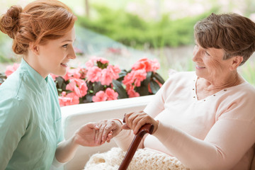 Canvas Print - Smiling caregiver supporting happy senior woman with walking stick