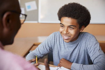 High School Tutor Giving Male Student One To One Tuition At Desk