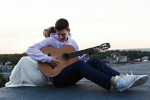 Man Plays A Guitar While His Woman Leans To Him Tender On The Rooftop